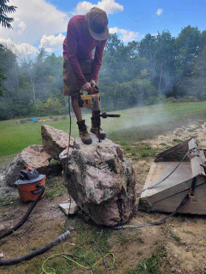 Crew member drilling a natural boulder to create a custom bubbling rock fountain